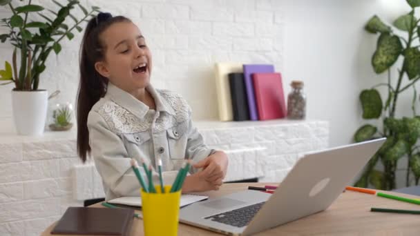 Niño en línea. Una niña utiliza una computadora portátil de chat de vídeo para comunicar el aprendizaje mientras está sentado en casa. — Vídeos de Stock