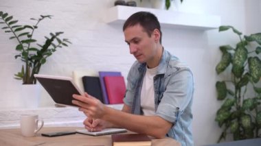 Evdeki masada tabletle çalışan adam.