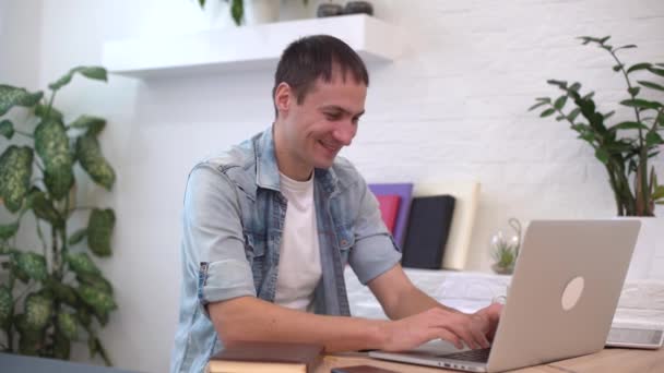 Портрет чоловіка, який працює вдома на якомусь проекті, він сидить за столом, малюючи ідеї на блокноті, з ноутбуком перед ним . — стокове відео