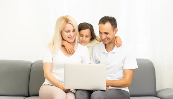 Familia feliz con niña divirtiéndose usando el ordenador portátil juntos sentados en el sofá, los padres y la hija se ríen relajándose en casa con la computadora viendo videos divertidos de Internet, haciendo llamadas en línea — Foto de Stock