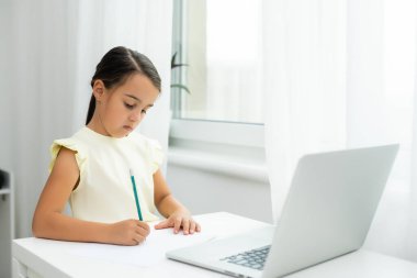 Küçük kız şaşırmış ve heyecanlı bir ifadeyle dizüstü bilgisayara bakıyor. Zeki, gülümseyen küçük kız notlar alıyor. İş konseptinde iletişim.