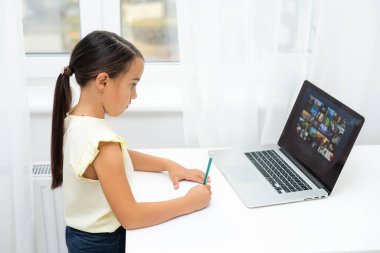 Küçük kız şaşırmış ve heyecanlı bir ifadeyle dizüstü bilgisayara bakıyor. Zeki, gülümseyen küçük kız notlar alıyor. İş konseptinde iletişim.