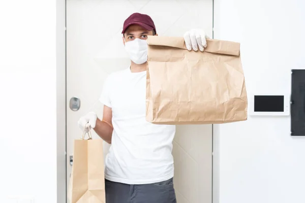 Futár, futár orvosi gumikesztyűben és maszkban biztonságosan szállít online vásárlásokat fehér dobozban az ajtónak a koronavírus járvány idején, a COVID-19-en. Maradj otthon, biztonságos koncepció.. — Stock Fotó