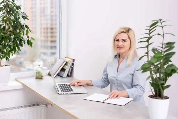 Confiante sério experiente qualificado bela mulher inteligente com cabelo loiro vestindo camisa está digitando cartas para seus clientes e parceiros de negócios, sentado à mesa no escritório — Fotografia de Stock