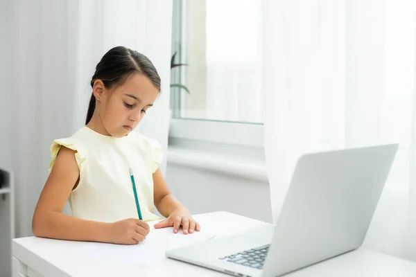 Menina minúscula olhando para a tela do laptop com expressão de surpresa e emoção. Uma menina esperta e sorridente a tirar apontamentos. Comunicação no conceito de negócio. — Fotografia de Stock