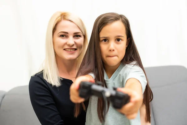 Buon rapporto carino bambina con la giovane madre utilizzando joystick giocare video gioco seduti insieme in soggiorno godendo vacanza in famiglia. — Foto Stock