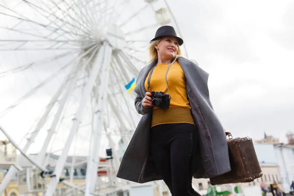Junge Frau mit Hut spaziert auf der Stadtstraße in der Nähe des Riesenrads und lächelt fröhlich. — Stockfoto