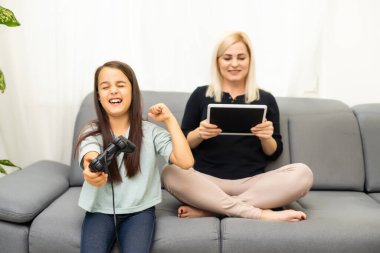 Mutlu bir aileyiz. Anne ve kız çocuğu video oyunu oynuyorlar. Aile rahatlar.