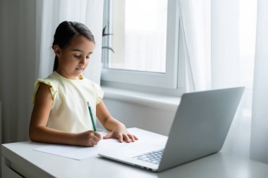 Küçük kız şaşırmış ve heyecanlı bir ifadeyle dizüstü bilgisayara bakıyor. Zeki, gülümseyen küçük kız notlar alıyor. İş konseptinde iletişim.