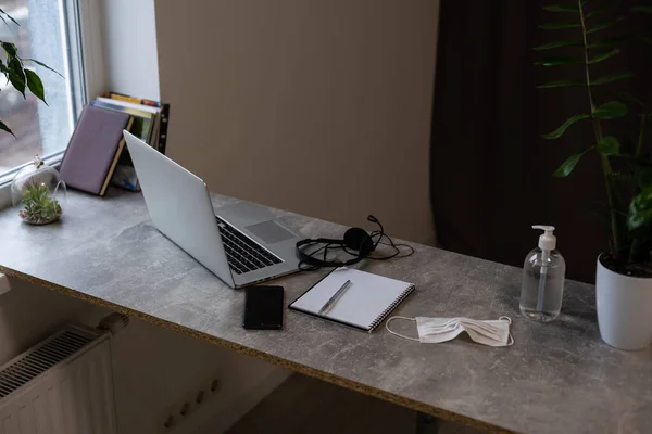 Lugar de trabalho na mesa cinza com computador portátil verde Flor vermelho cadeira e lápis no interior do escritório moderno com grande janela no fundo — Fotografia de Stock