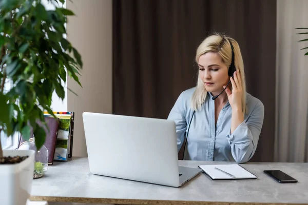 Egy fiatal nő ül az asztalánál egy szürke laptop előtt, miközben szép emlékekről vagy jövőről álmodozik egy modern, fényes irodában, nagy ablakkal. — Stock Fotó