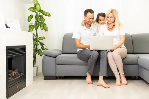 Famille heureuse avec enfant fille s'amuser à l'aide d'un ordinateur portable assis sur le canapé, les parents et la fille enfant rire relaxant à la maison avec ordinateur regarder drôle de vidéo sur Internet, faire appel en ligne — Photo