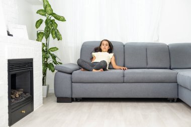 Küçük kız kanepede oturuyor ve bir şeye üzülüyor.