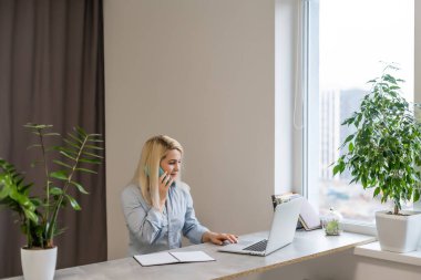 Gri bir dizüstü bilgisayarın önünde masasında oturan genç bir kadın güzel anılar ya da büyük pencereli modern parlak bir ofiste geleceği düşlüyor.