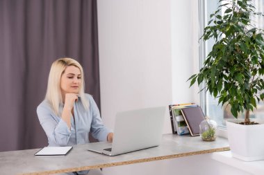 Kendine güvenen, tecrübeli, sarışın, zeki ve sarışın bir kadın müşterilerine ve iş ortaklarına mektup yazıyor. Ofiste masada oturuyor.