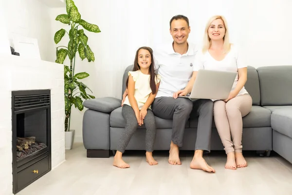 Famille heureuse avec enfant fille s'amuser à l'aide d'un ordinateur portable assis sur le canapé, les parents et la fille enfant rire relaxant à la maison avec ordinateur regarder drôle de vidéo sur Internet, faire appel en ligne — Photo