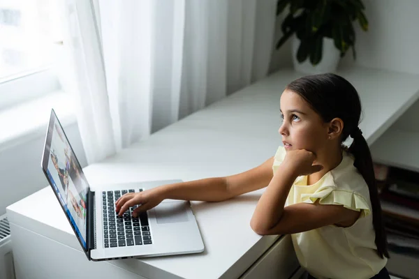 Klein meisje op zoek naar laptop scherm met expressie van verrast en opwinding. Slim, lachend meisje dat aantekeningen maakt. Communicatie in het bedrijfsleven. — Stockfoto