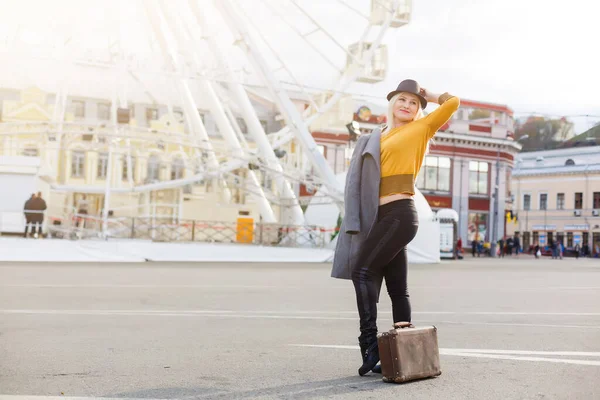 Mujer joven con sombrero caminando al aire libre en la calle de la ciudad cerca de la noria sonriente alegre. — Foto de Stock