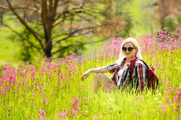 ピンクのシャクナゲの花の間の緑の山の斜面に幸せな冒険家の女性が立っているとの距離を調べる。山の中で壮大な旅行。広角. — ストック写真
