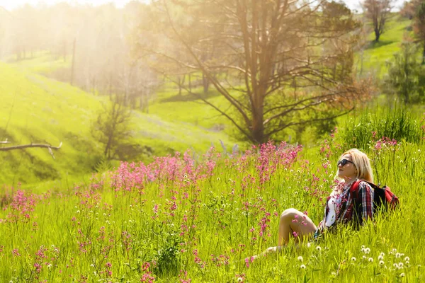 Feliz aventureiro fêmea fica na encosta da montanha verde entre rododendros rosa floridos e olhando para a distância. Viagens épicas nas montanhas. Ângulo largo. — Fotografia de Stock