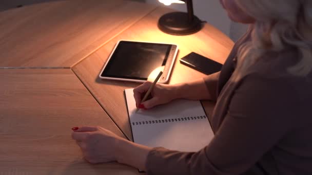 Sorrindo mulher atraente pensando em algo, em seguida, escrever algo no caderno enquanto sentado à mesa — Vídeo de Stock