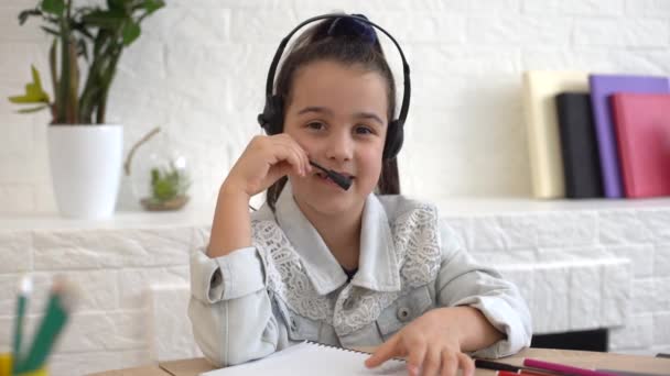 Το χαρούμενο κορίτσι με τα ακουστικά με το λάπτοπ να κάθεται στο τραπέζι — Αρχείο Βίντεο
