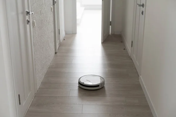 White robotic vacuum cleaner on laminate floor cleaning dust in living room interior. Smart housekeeping technology.