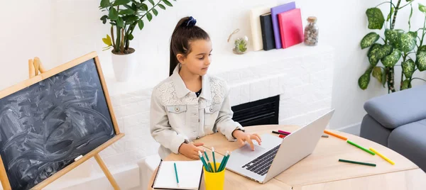 Pequeña niña inteligente aprende en línea en un ordenador portátil, video chat en casa, educación a distancia —  Fotos de Stock