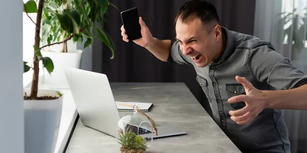 Молодий шокований чоловік одягнений у сорочку, використовуючи ноутбук. на сірому . — стокове фото