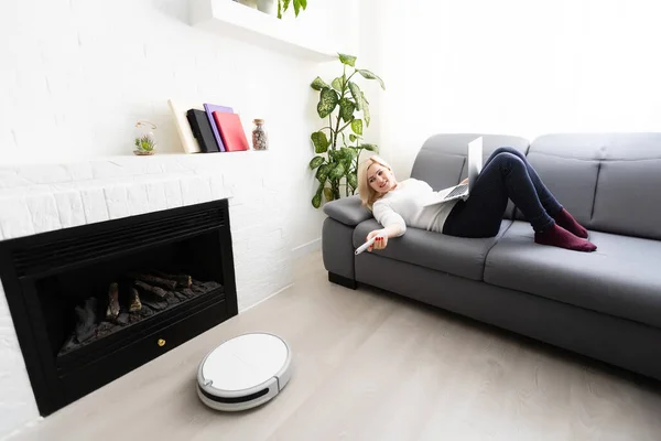 Robotic dammsugare städa rummet medan kvinnan sitter på soffan, närbild — Stockfoto