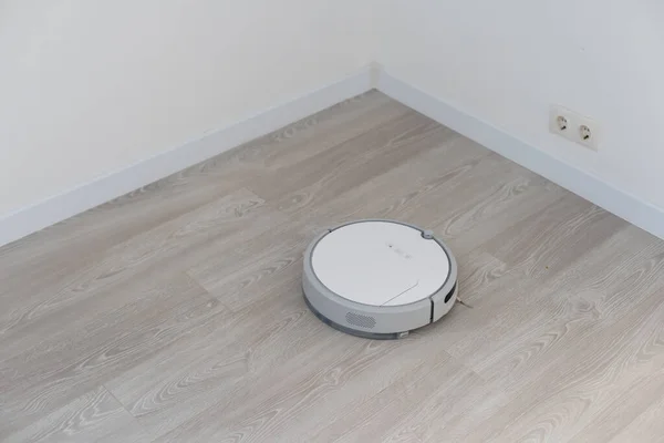 Aspiradora robótica blanca en polvo de limpieza de suelo laminado en el interior de la sala de estar. Tecnología inteligente de limpieza. — Foto de Stock