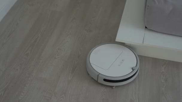 Bílý robotický vysavač na laminátové podlaze čistící prach v interiéru obývacího pokoje. Inteligentní technologie pro vedení domácnosti. — Stock video