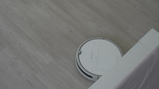 Bílý robotický vysavač na laminátové podlaze čistící prach v interiéru obývacího pokoje. Inteligentní technologie pro vedení domácnosti. — Stock video