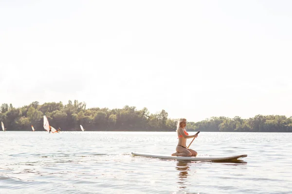 Mujer con una pala en la pizarra. piernas de una chica delgada en stand up paddle board. — Foto de Stock