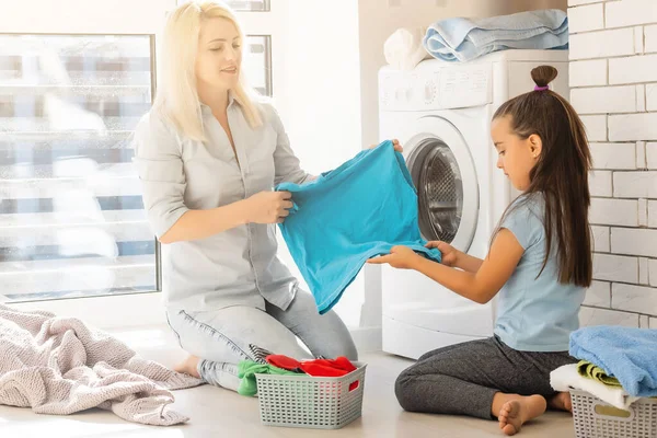 Mutlu ev hanımı ve kızı çamaşır makinesinin yanında çarşaf taşıyor. — Stok fotoğraf