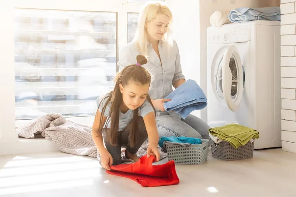Aile annesi ve kız çocuğu çamaşır odasında çamaşır makinesi ve kirli çamaşırların yanında. — Stok fotoğraf