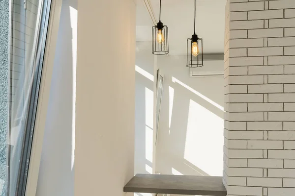 Duas lâmpadas de aço iluminam uma mesa de bar contra uma parede em um estilo minimalista moderno com uma cor branca na parede acima do contador e marrom abaixo — Fotografia de Stock