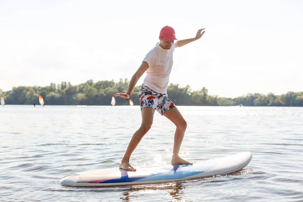 Retrato de un surfista con una tabla SUP en la playa. Joven en el paddleboard al amanecer. El concepto de deportes extremos. Estilo de vida del surfista masculino. —  Fotos de Stock