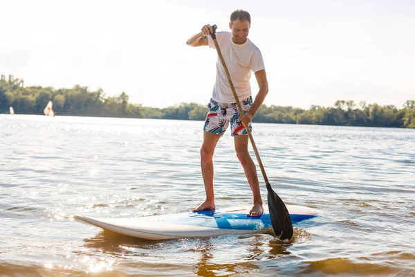 Silueta de stand up paddle boarder remando al atardecer —  Fotos de Stock