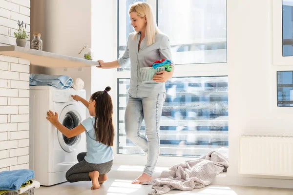 Feliz ama de casa y su hija con ropa de cama cerca de la lavadora — Foto de Stock