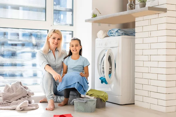 Feliz ama de casa y su hija con ropa de cama cerca de la lavadora — Foto de Stock