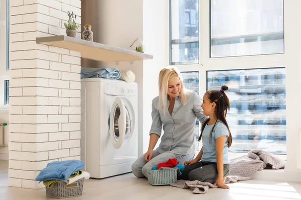Šťastná hospodyňka a její dcera s ložním prádlem v blízkosti pračky — Stock fotografie