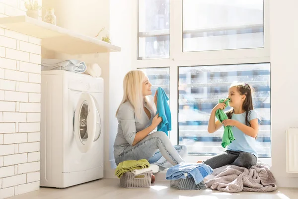 Šťastná hospodyňka a její dcera s ložním prádlem v blízkosti pračky — Stock fotografie