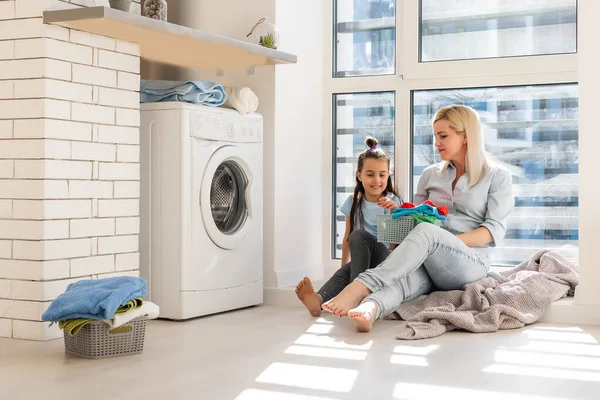 Feliz ama de casa y su hija con ropa de cama cerca de la lavadora — Foto de Stock