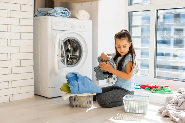 Krásné dítě dívka malý pomocník se baví a hraje při praní prádla doma. — Stock fotografie