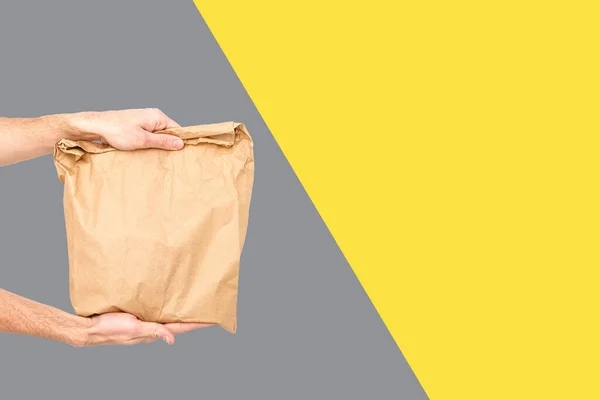 Cerrar hembra sostiene en mano marrón claro vacío vacío bolsa de papel artesanal para llevar Concepto de servicio de entrega. Copiar espacio. Colores de moda 2021 - Gris y Amarillo. —  Fotos de Stock