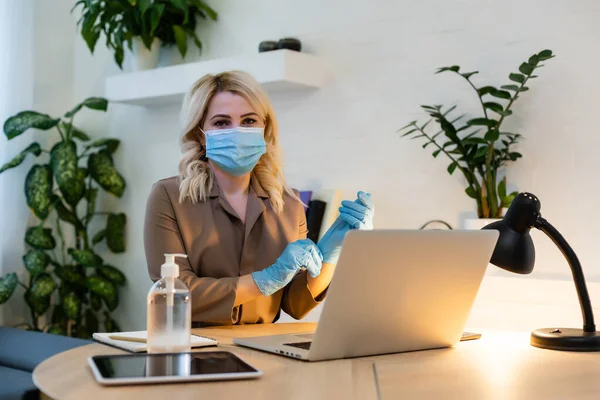 En la oficina. mujer con mascarilla facial, el desinfectante está junto a la mesa — Foto de Stock