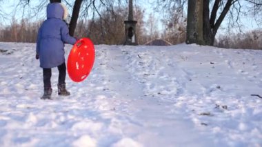 Küçük kız kar kaplı tepede buz kızağında yokuş aşağı gidiyor.