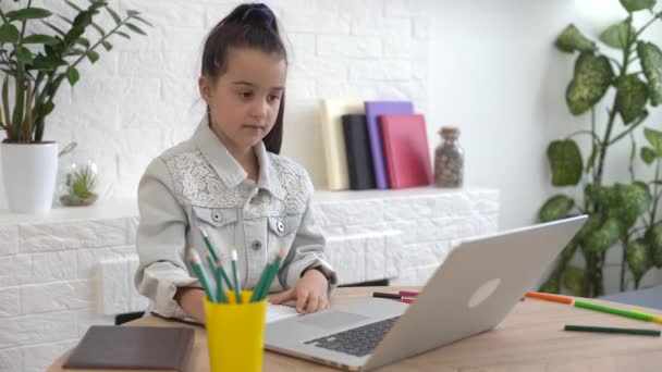 Niño en línea. Una niña utiliza una computadora portátil de chat de vídeo para comunicar el aprendizaje mientras está sentado en casa. — Vídeos de Stock