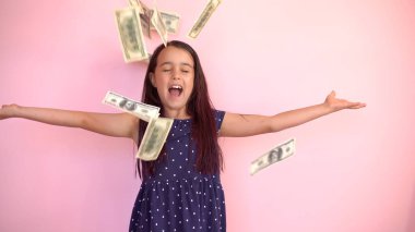 Dolarları tutan sevimli küçük bir kız, pembe üzerine izole edilmiş.